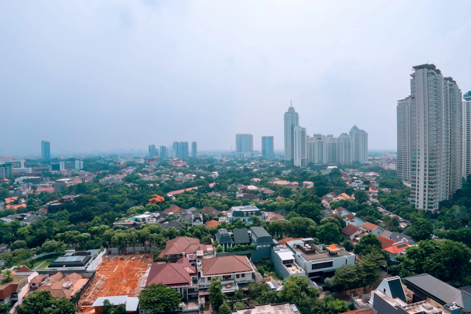 Lanskap Kota Jakarta dilihat dari ketinggian: deretan gedung bertingkat dan permukiman padat yang diselimuti kabut polusi.