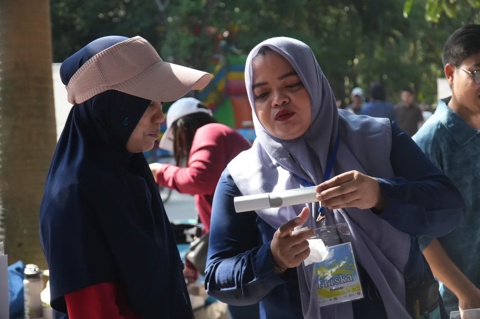 Seorang tenaga kesehatan perempuan memberikan instruksi kepada seorang perempuan paruh baya untuk meniup peak flow meter.