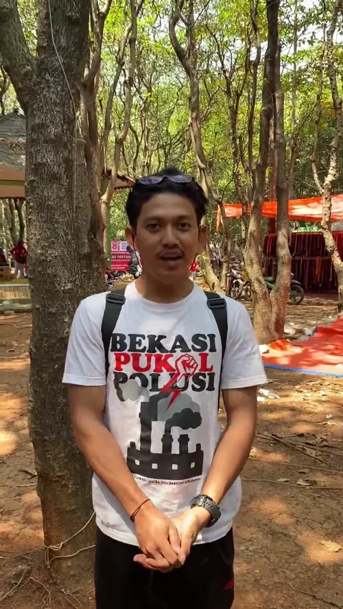 Shihabuddin dari Bekasi Pukul Polusi berdiri di area berpohon Hutan Kota Bekasi, mengenakan kaus putih bertuliskan Bekasi Pukul Polusi.