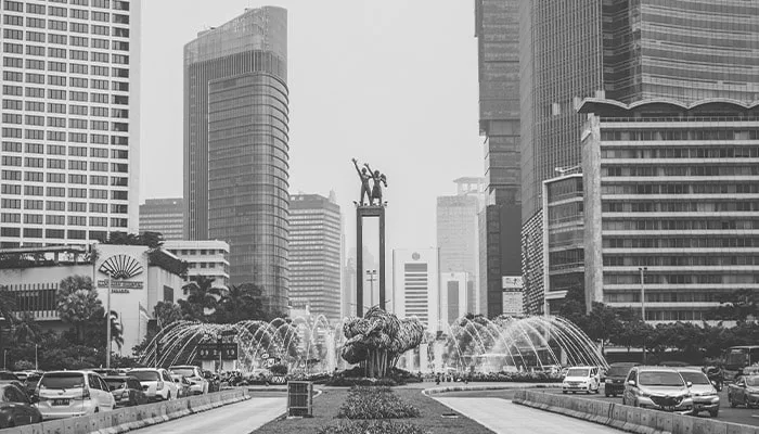 Foto hitam putih lanskap kota Jakarta dengan deretan gedung pencakar langit mengelilingi Tugu Selamat Datang di Bundaran HI.