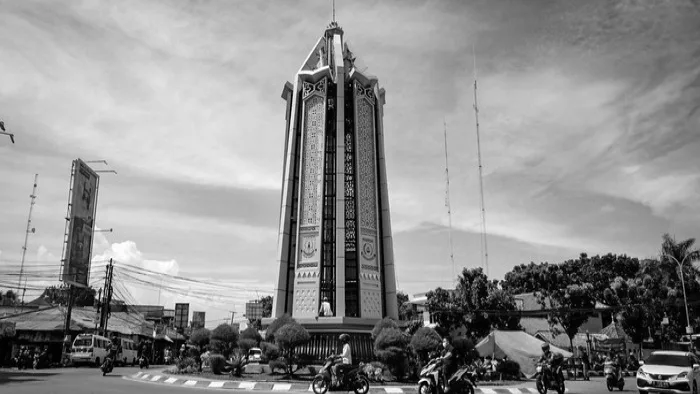 Foto hitam putih tugu di persimpangan jalan Kota Tangerang Selatan dengan langit berawan di latar belakang.